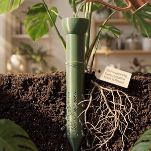Op de afbeelding: Een cilindervormige groene 3D-geprinte PETG-plantenwatergeefstaaf in donkere aarde, met een trechtervormige bovenkant en geperforeerde zijkanten voor waterafgifte. Een klein rechthoekig label met de tekst 3D Printed PETG Deep Hydration Made in Poland.