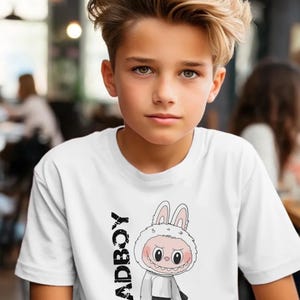 May include: White t-shirt featuring a cartoon character in a bunny costume with the word "BADBOY" printed vertically on the left side. The character is wearing a hoodie, black pants, and sneakers.