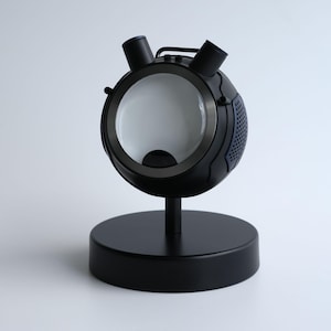 May include: A black desk lamp with a spherical head, two cylindrical elements, and a circular base. The lamp has a large, round, white interior and a small, black stand. The design is modern and minimalist.