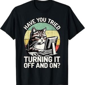 May include: A black short-sleeved t-shirt featuring a graphic of a tabby cat sitting at a computer. The text reads HAVE YOU TRIED TURNING IT OFF AND ON? The design includes a distressed circular background with yellow, orange, and green horizontal stripes.
