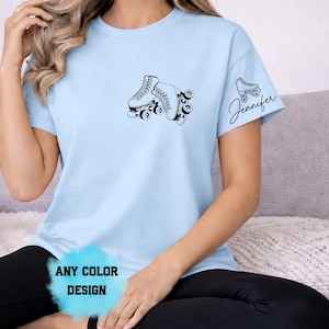 May include: Light blue t-shirt featuring a black graphic of roller skates. The shirt has the text "Jennifer" on the sleeve. The text "ANY COLOR DESIGN" is also visible on the shirt.