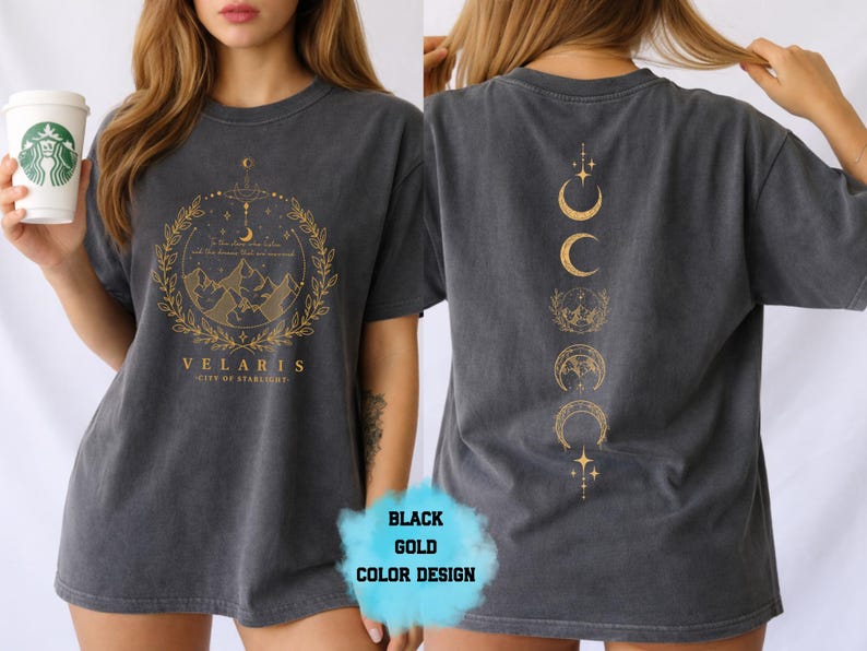 Pode incluir: Camiseta cinza escuro com gr&aacute;ficos dourados na frente e nas costas. O design frontal apresenta uma cena de montanha dentro de uma coroa, com o texto "VELARIS - CITY OF STARLIGHT". A parte de tr&aacute;s tem um design vertical de luas e estrelas.
