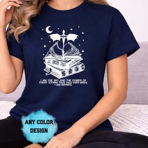 May include: Navy blue t-shirt with a white graphic of books, a dragon, and a crescent moon. The text reads "I AM THE SKY AND THE POWER OF EVERY STORM THAT HAS EVER BEEN. I AM INFINITE."