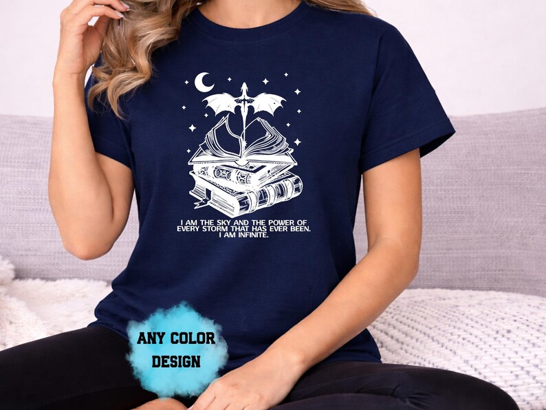 May include: Navy blue t-shirt with a white graphic of books, a dragon, and a crescent moon. The text reads "I AM THE SKY AND THE POWER OF EVERY STORM THAT HAS EVER BEEN. I AM INFINITE."