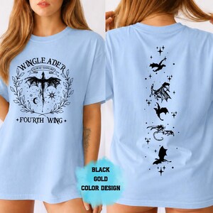 May include: Light blue t-shirt with a black graphic design. The front features a winged creature within a wreath, with text reading "WINGLEADER" and "FOURTH WING." The back displays a vertical line of dragon silhouettes. "BLACK GOLD COLOR DESIGN" text is also present.