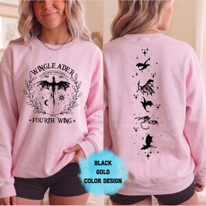 May include: A light pink sweatshirt with black dragon graphics. The front features a dragon design with the text "WINGLEADER" and "FOURTH WING". The back has a vertical line of dragon silhouettes. The design is in black and gold.