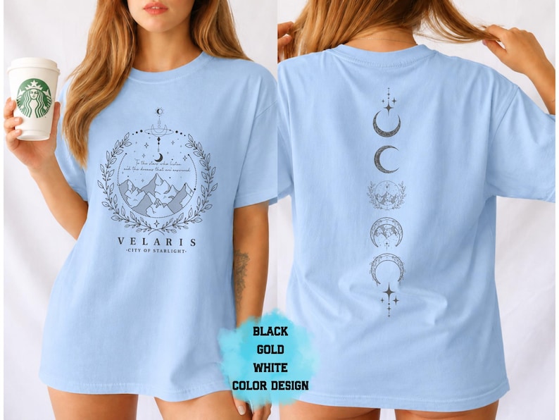 Pode incluir: Camiseta azul clara com um gr&aacute;fico frontal com montanhas, uma lua crescente e o texto "VELARIS - CITY OF STARLIGHT". A parte de tr&aacute;s da camisa exibe um design vertical de luas crescentes e estrelas. Dispon&iacute;vel em preto, dourado e branco.