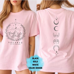 Pode incluir: Camiseta rosa claro com um design gr&aacute;fico na frente e atr&aacute;s. A frente apresenta uma paisagem montanhosa dentro de uma moldura circular com o texto "VELARIS - CITY OF STARLIGHT". A parte de tr&aacute;s exibe uma disposi&ccedil;&atilde;o vertical das fases da lua. O texto "BLACK GOLD WHITE COLOR DESIGN" tamb&eacute;m &eacute; vis&iacute;vel.