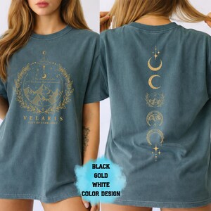 Pode incluir: Camiseta azul-petr&oacute;leo com um gr&aacute;fico dourado na frente com montanhas, uma lua crescente e a palavra "VELARIS". A parte de tr&aacute;s da camisa exibe um design vertical de luas crescentes e estrelas douradas. A camiseta &eacute; de estilo casual.