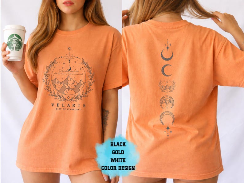 Pode incluir: Camiseta laranja com um gr&aacute;fico frontal com montanhas, uma lua crescente e o texto "VELARIS - CITY OF STARLIGHT". A parte de tr&aacute;s da camisa exibe um design vertical de fases lunares. A camisa tem um ajuste folgado.