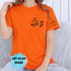 May include: Bright orange t-shirt featuring a black roller skate design on the front and a smaller skate with the name "Jennifer" on the sleeve. The shirt has a crew neck and short sleeves. The text "ANY COLOR DESIGN" is also visible.