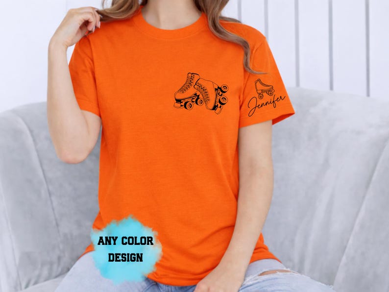 May include: Bright orange t-shirt featuring a black roller skate design on the front and a smaller skate with the name "Jennifer" on the sleeve. The shirt has a crew neck and short sleeves. The text "ANY COLOR DESIGN" is also visible.