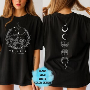 Pode incluir: Camiseta preta com um gr&aacute;fico branco na frente com montanhas, estrelas e o texto "VELARIS - CITY OF STARLIGHT". A parte de tr&aacute;s da camisa tem um design vertical de fases da lua. Dispon&iacute;vel em preto, dourado e branco.