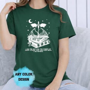 May include: Dark green t-shirt with a white graphic of books, a dragon, a crescent moon, and stars. The text on the shirt reads "I AM THE SKY AND THE POWER OF EVERY STORM THAT HAS EVER BEEN. I AM INFINITE." The shirt also says "ANY COLOR DESIGN."