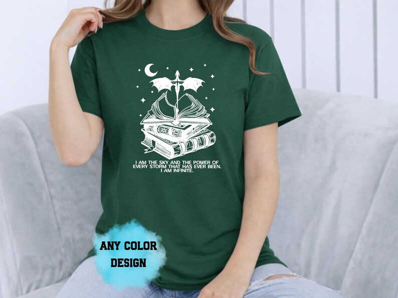 May include: Dark green t-shirt with a white graphic of books, a dragon, a crescent moon, and stars. The text on the shirt reads "I AM THE SKY AND THE POWER OF EVERY STORM THAT HAS EVER BEEN. I AM INFINITE." The shirt also says "ANY COLOR DESIGN."