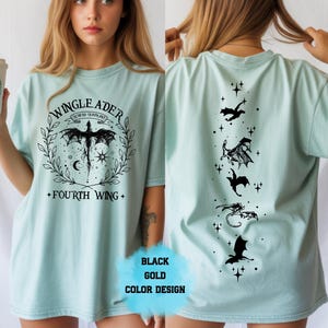 Op de afbeelding: Lichtblauw T-shirt met een zwart grafisch ontwerp. De voorkant heeft een drakenontwerp met de tekst "WINGLEADER" en "FOURTH WING". De achterkant heeft drakensilhouetten en sterren. "BLACK GOLD COLOR DESIGN" is ook zichtbaar.