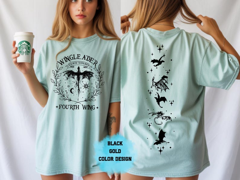 Op de afbeelding: Lichtblauw T-shirt met een zwart grafisch ontwerp. De voorkant heeft een drakenontwerp met de tekst "WINGLEADER" en "FOURTH WING". De achterkant heeft drakensilhouetten en sterren. "BLACK GOLD COLOR DESIGN" is ook zichtbaar.