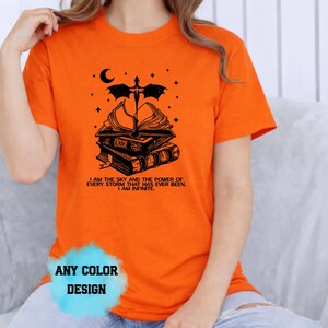 May include: Orange t-shirt with a black graphic of stacked books, a dragon, moon, and stars. Text on the shirt reads "I AM THE SKY AND THE POWER OF EVERY STORM THAT HAS EVER BEEN. I AM INFINITE." The shirt design is available in any color.