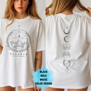 Pode incluir: Camiseta branca com um gr&aacute;fico frontal com montanhas, uma lua crescente e o texto "VELARIS - CITY OF STARLIGHT". A parte de tr&aacute;s da camisa exibe uma s&eacute;rie de fases da lua.