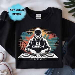 Könnte beinhalten: Schwarzes Sweatshirt mit einem DJ-Grafik, Kopfhörern und einem Mischpult. Das Design enthält den Text "DJ CUSTOM" und einen bunten Backsteinmauer-Hintergrund. Die Worte "ANY COLOR DESIGN" sind ebenfalls vorhanden.