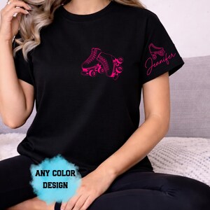 May include: Black t-shirt with a pink roller skate graphic on the front and a smaller skate and the name "Jennifer" on the sleeve. The text "ANY COLOR DESIGN" is also visible. The shirt is made of a soft material.
