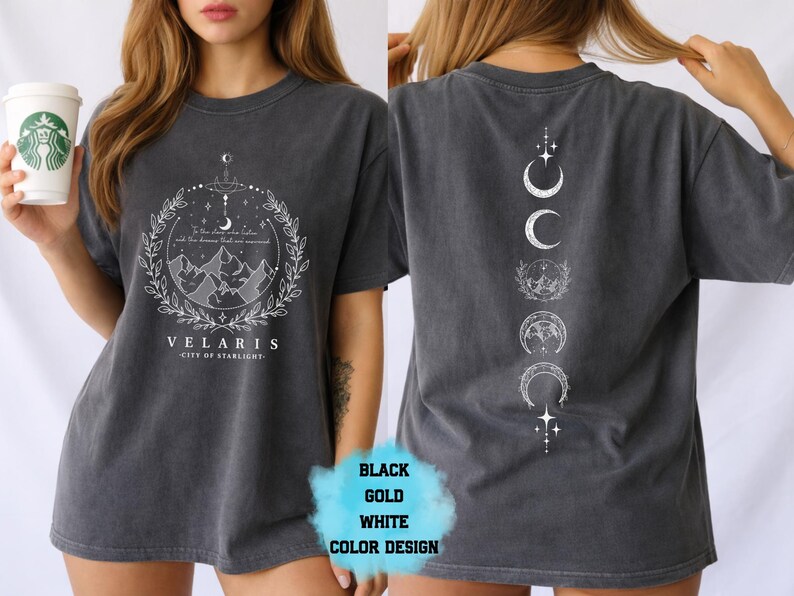 Pode incluir: T-shirt cinza escuro com um gr&aacute;fico branco na frente com montanhas, estrelas e o texto "VELARIS - CITY OF STARLIGHT". A parte de tr&aacute;s da camisa tem um design vertical de fases da lua. A camisa &eacute; um estilo unissex.