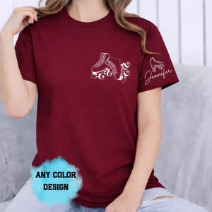 May include: Burgundy t-shirt with a white roller skate graphic on the chest and sleeve. The sleeve also features the name "Jennifer" in script. The shirt has a crew neck and short sleeves. The bottom of the shirt has a blue and white graphic that says "ANY COLOR DESIGN".