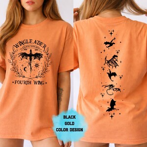 Op de afbeelding: Oranje t-shirt met zwart grafisch ontwerp. Voorkant met een gevleugeld wezen, tekst "WINGLEADER" en "FOURTH WING". Achterkant met draken silhouetten en sterren. Zwart en goud kleurontwerp.