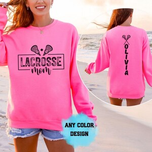 Sudadera con capucha personalizada con nombre de mamá de lacrosse, estilo retro, con marco de caja, insignia, texto en cursiva, palo de pelota, diseño gráfico llamativo.