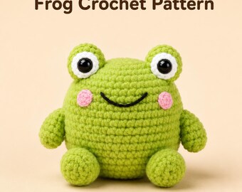 May include: A round, light green crocheted frog plush toy with large black and white eyes, a black stitched smile, and small pink cheeks. The text "Frog Crochet Pattern" is displayed in dark brown letters above the stuffed animal figure.
