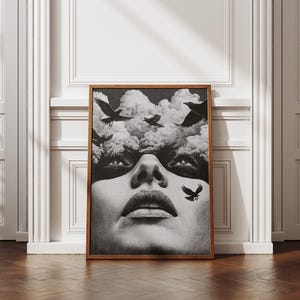 May include: A monochrome framed art print depicting a woman's face, clouds, and birds. The artwork has a surreal, dreamlike quality. The wooden frame adds a classic touch to the piece, suitable for home decor.