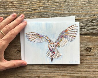 May include: A rectangular greeting card featuring a watercolor illustration of a barn owl in flight with wings spread wide. The owl is rendered in shades of white, brown, and orange with colorful accents. The artist's signature is in the bottom right.