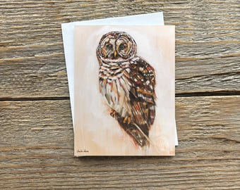 May include: A rectangular greeting card featuring a painted illustration of a barred owl with brown, white, and black feathers. The owl is depicted against a light beige background. The artist's signature is visible in the bottom left corner.