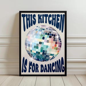 May include: A framed print with a black border features a disco ball illustration. The words "THIS KITCHEN IS FOR DANCING" are in navy blue, arched above and below the disco ball. The disco ball is a mosaic of colorful squares.
