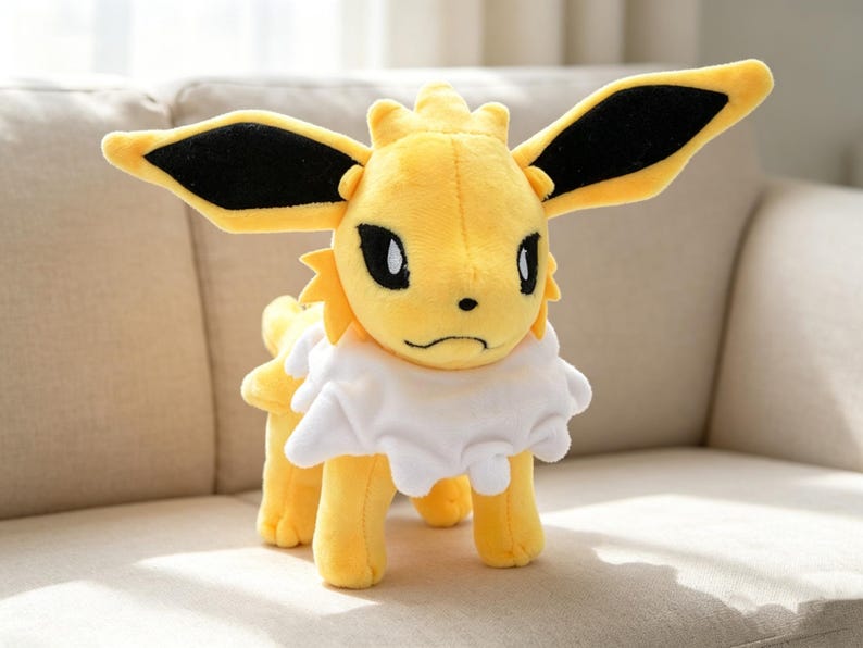 May include: A plush toy of a yellow creature with large, black-tipped ears, black eyes, and a white ruffled collar. The toy is standing on four legs and has a slightly grumpy expression. The toy is a popular character from a well-known franchise.