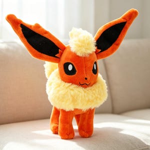 May include: A plush toy of a character with orange fur, large ears with black accents, and a fluffy yellow mane and collar. The toy has black eyes and is standing on a beige couch.