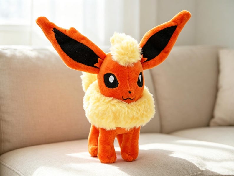 May include: A plush toy of a character with orange fur, large ears with black accents, and a fluffy yellow mane and collar. The toy has black eyes and is standing on a beige couch.