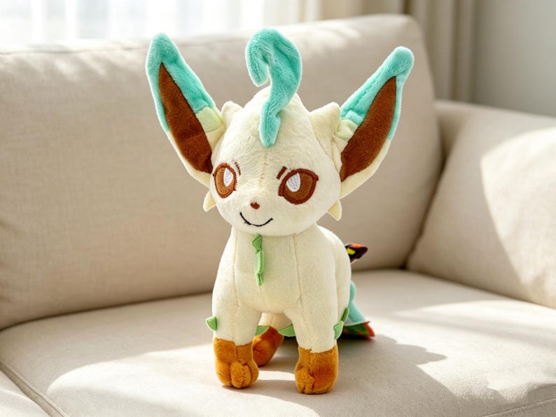 May include: A plush toy of a character with cream-colored fur, brown eyes, and orange feet. The character has large ears with brown and teal accents, and a teal curl on its head. It is sitting on a beige couch.