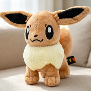 May include: A plush Eevee toy, featuring brown fur, large ears with black tips, and a fluffy cream-colored ruff. The toy has large, expressive eyes and a small, black nose and mouth. It is posed on a neutral-toned sofa.