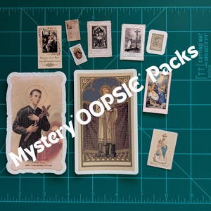 May include: A collection of religious cards and stickers, featuring various saints and biblical scenes. The cards vary in size and design, with images of religious figures and text. The background is a green cutting mat with grid lines, and the text "Mystery Oopsic Packs".