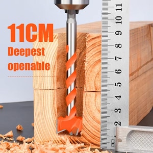 Könnte beinhalten: Ein Bohrer mit orangefarbenem Schneidkopf ist in einen Holzblock eingesetzt. Der Text "11CM Deepest openable" ist orange dargestellt. Ein Metalllineal befindet sich neben dem Bohrer.