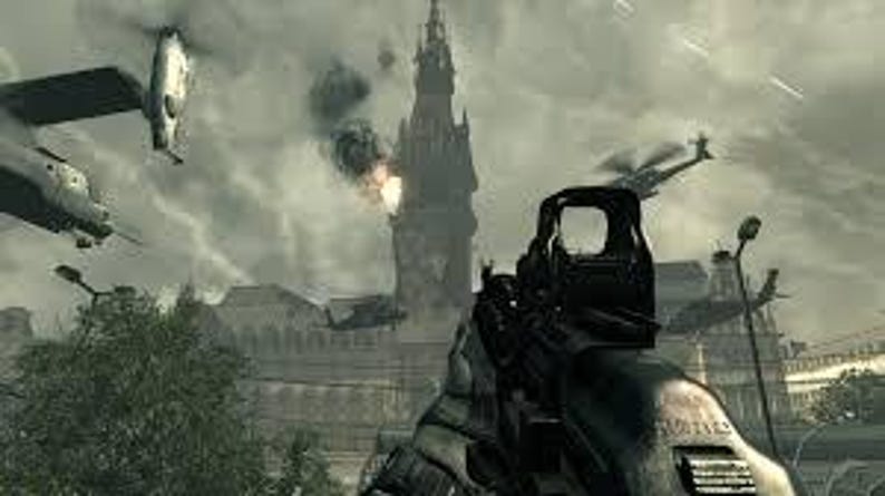K&ouml;nnte beinhalten: Ego-Perspektive aus einem Videospiel, mit dem Visier einer Waffe auf ein entferntes Geb&auml;ude gerichtet. Hubschrauber und Flugzeuge sind am Himmel zu sehen, mit Explosionen und Rauch. Die Szene spielt in einer kriegszerst&ouml;rten Umgebung.