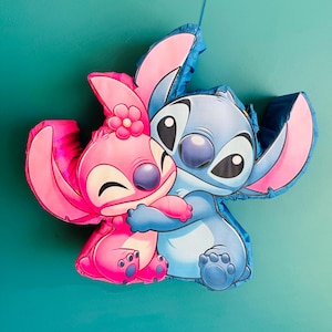 May include: A blue and pink pi&ntilde;ata depicting the characters Stitch and Angel from Lilo & Stitch. Angel, in pink, embraces Stitch, who is blue. The pi&ntilde;ata is set against a teal backdrop.