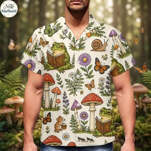 May include: A short-sleeve button-down shirt in cream featuring a repeating pattern of green frogs reading books, various colorful mushrooms, orange and green butterflies, small brown mice, and purple and white flowers across the fabric.