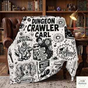 May include: A white throw blanket featuring black line art illustrations and text related to Dungeon Crawler Carl. The design includes characters like a cat, a dinosaur, and a person, along with phrases such as This Is An Outrage and Donut.