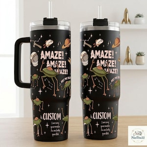 May include: A black stainless steel tumbler with a handle and straw, featuring a space-themed pattern with planets, stars, and alien creatures. The text reads 'AMAZE! AMAZE! AMAZE!', 'FIST MY BUMP', 'CUSTOM', and 'I am scary space monster. You are leaky space blob.'