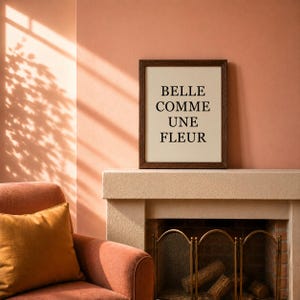 Peut inclure: Une affiche rectangulaire dans un cadre en bois brun foncé avec le texte noir BELLE COMME UNE FLEUR centré sur un fond crème. L'affiche est posée sur une cheminée de couleur claire au-dessus d'un foyer.