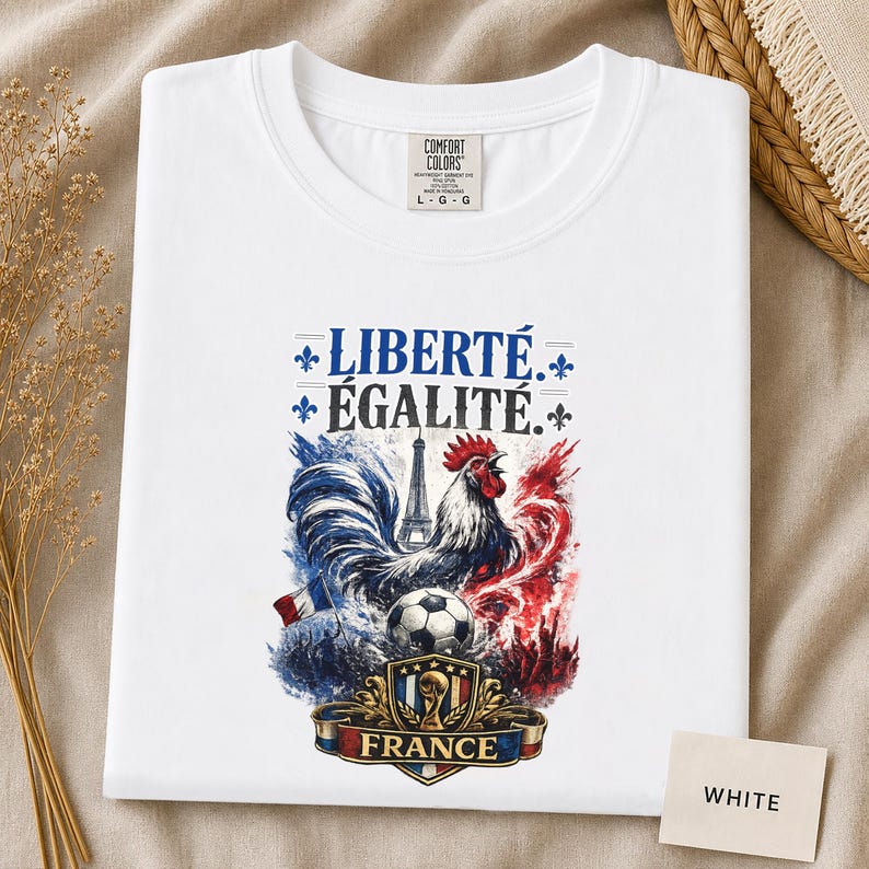 Puede incluir: Una camiseta blanca con un estampado gr&aacute;fico que incluye el texto LIBERT&Eacute; &Eacute;GALIT&Eacute;. El dise&ntilde;o muestra un gallo, la Torre Eiffel, un bal&oacute;n de f&uacute;tbol y un escudo con la palabra FRANCE, todo en salpicaduras de estilo acuarela azul, blanco y rojo.