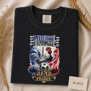 Puede incluir: Una camiseta negra con un estampado gr&aacute;fico que incluye el texto LIBERT&Eacute; &Eacute;GALIT&Eacute;, un gallo, la Torre Eiffel, un bal&oacute;n de f&uacute;tbol y un escudo con la palabra FRANCE. La camiseta tiene una etiqueta de la marca Comfort Colors en el cuello.