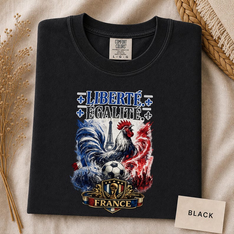 Puede incluir: Una camiseta negra con un estampado gr&aacute;fico que incluye el texto LIBERT&Eacute; &Eacute;GALIT&Eacute;, un gallo, la Torre Eiffel, un bal&oacute;n de f&uacute;tbol y un escudo con la palabra FRANCE. La camiseta tiene una etiqueta de la marca Comfort Colors en el cuello.